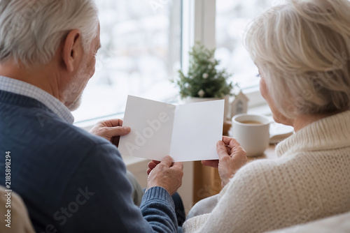 窓辺で白紙カードを確認するシニア夫婦