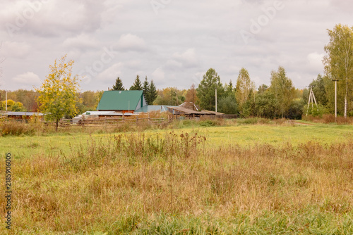 View of village buildings and a fence across a field of tall, dry autumn grass