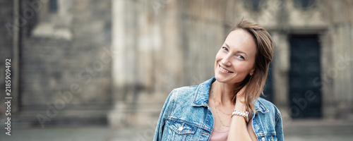 Portrait smiling young adult cheerful woman wear denim jacket historic European city Magdeburg stone gothic architecture background. Candid female person relax travel authentic lifestyle urban charm