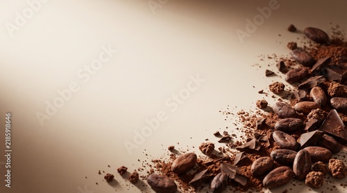 Rich chocolate background featuring cocoa beans, chocolate pieces and cocoa powder arranged on a rustic surface with warm natural lighting and spacious copy space.