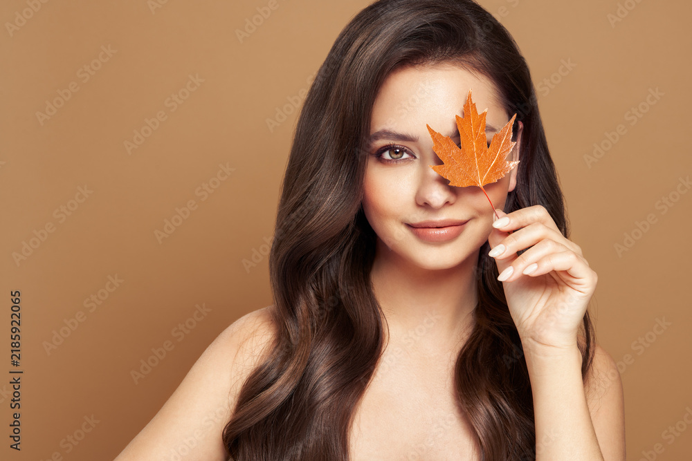 Obraz premium Portrait of beautiful young woman with autumn leafs. Healthy clean fresh skin natural make up.Long curly hairstyle. Care and beauty hair products