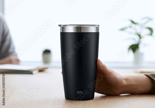 A matte black insulated tumbler with a silver rim, held by a hand