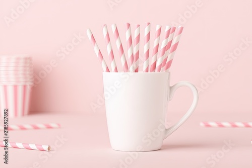 Pink and white striped straws in a white mug on a pastel background