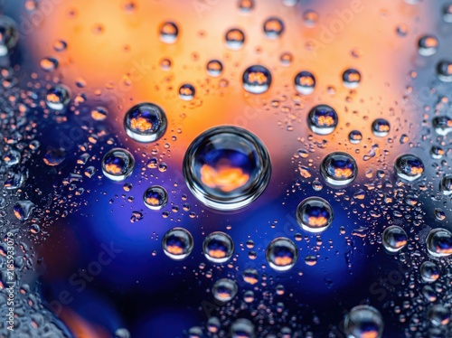 Abstract water droplets on glass surface, vibrant orange and blue bokeh background, macro condensation texture for creative design
