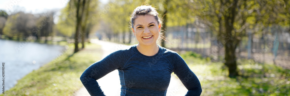 Obraz premium Portrait auf a cheerful and happy smiling woman wearing sportswear outdoors in nature, panoramic view 