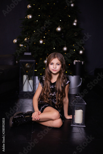 Charming little girl sitting on floor near decorative lantern and  Christmas tree