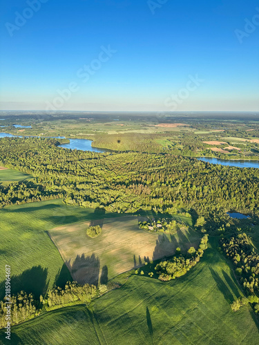 Aerial view of green farmland and forest under clear blue sky. Scenic countryside, summer landscape, rural travel, peaceful outdoors, wide view. Vertical background with copy space
