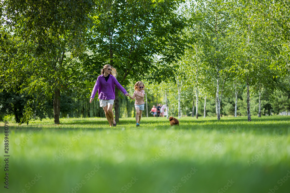 Fototapeta premium Mother and little girl holding hands and running across a green park lawn