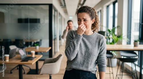 Young woman holding her nose because of a bad smell in the modern office.
