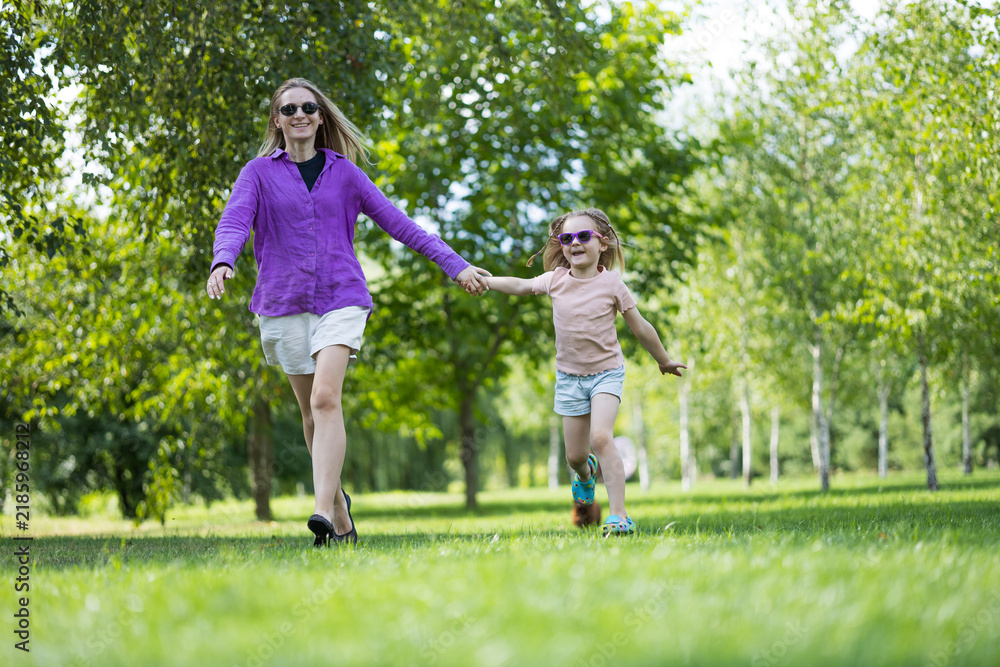 Fototapeta premium Mother and daughter walking towards camera hand in hand in park