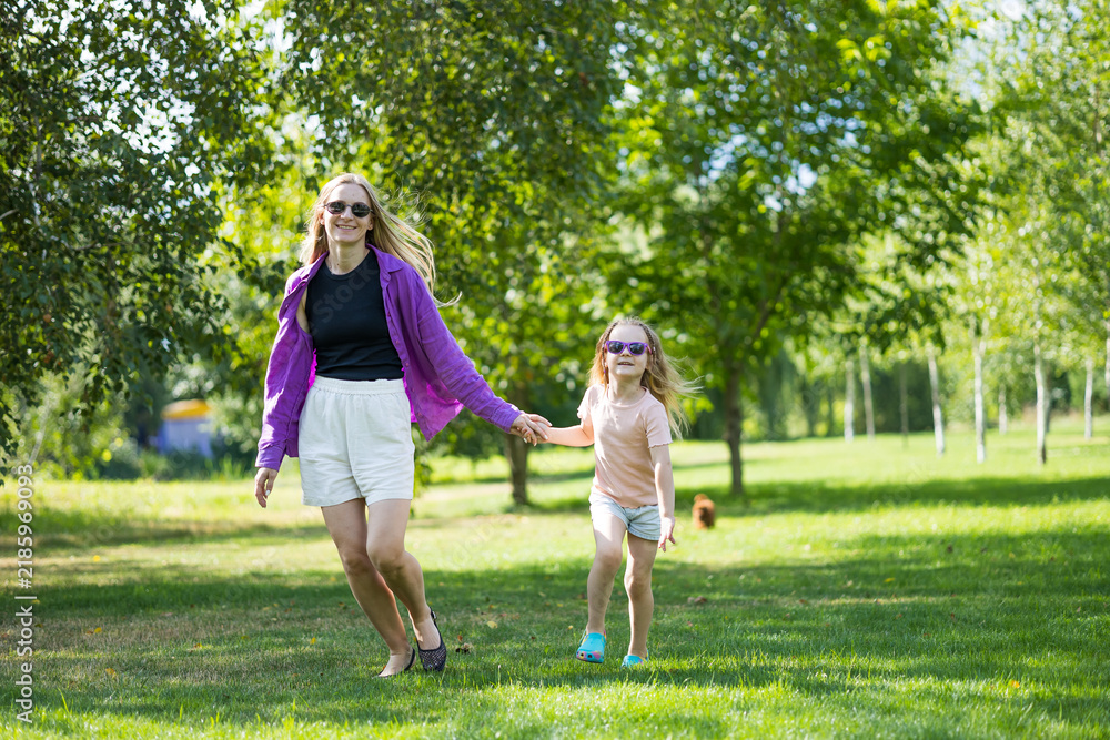 Fototapeta premium Mother and young daughter holding hands while walking on park grass outdoors
