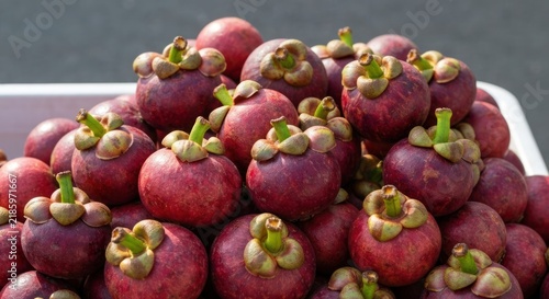 A close-up of a pile of purplish-red tropical fruit with green stems, in a white container