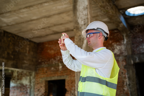 Construction professional using smartphone inside unfinished building site while wearing safety equipment. Digital construction management remote inspection and progress reporting