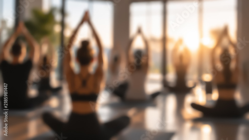 Blurred view of a group of people in lotus pose with raised arms during a yoga class
