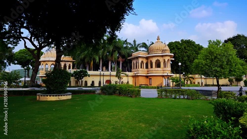 Udaipur, Rajasthan, India: Domed pavilions and yellow garden walls at Jag Mandir stand among palms and mature trees beside a neatly kept lawn.