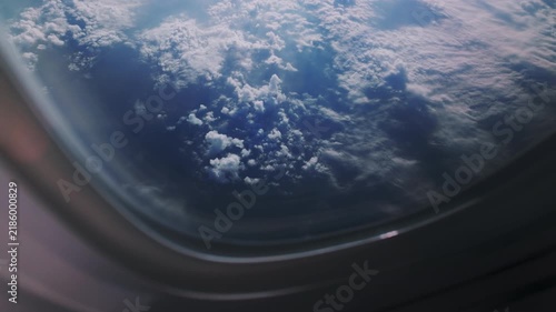 View of clouds and blue sky from an airplane window during a flight at daytime with sunlight shining