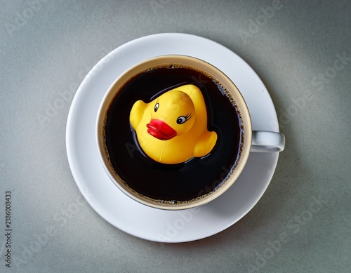 playful surreal concept photograph of a solid gold rubber duck floating in black coffee symbolizing luxury meets everyday life against a neutral background