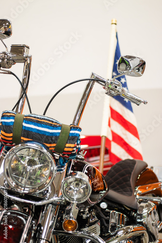Krakow, Polska - September 06, 2026: Custom motorcycle with chrome details and colorful seat cover, American flag displayed in the background, showcasing classic design elements