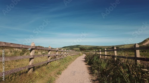 Pathway through green fields on a clear day with blue sky and distant hills in the background