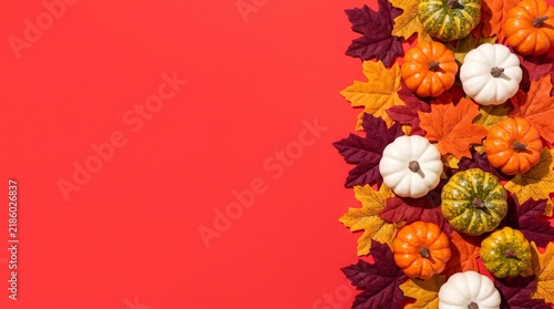 Small pumpkins and colorful autumn leaves arranged on a bright red background with pumpkins artificial maple