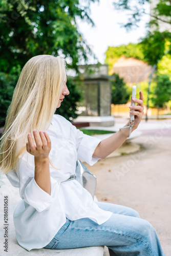 Young blonde woman taking selfie with smartphone in park
