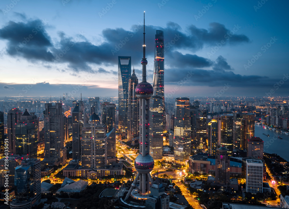 Obraz premium Aerial view of the Shanghai CBD skyline at dawn, featuring illuminated skyscrapers against a vibrant sunrise, symbolizing a global economic hub.