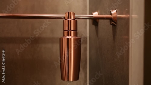 Copper cocktail shaker hanging on a copper bar in a modern bathroom with warm ambient lighting