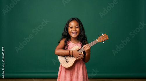 Joyful young girl with a ukulele, smiling widely with missing front teeth