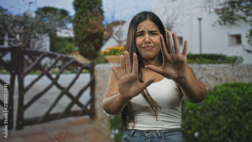 Canvastavla Young woman with palms out pushing away from a wooden gate at a building entrance, visible hands and a pained facial grimace; disgust refusal