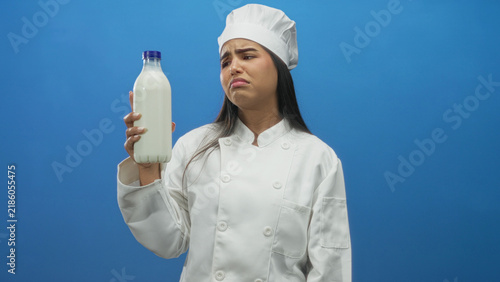 Fotografía Woman chef holds milk bottle up, grimacing while inspecting label in studio; hesitation reluctance disgust