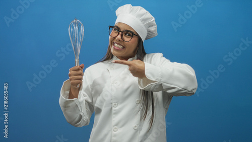 Cuadro en lienzo Chef woman points finger to stainless steel whisk and holds its handle in studio while smiling and wearing glasses; joy confidence celebration