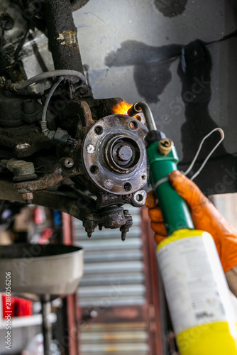 Bild auf Leinwand Mechanic using a handheld gas torch to heat a rusted component on a car’s wheel hub assembly during automotive repair and maintenance