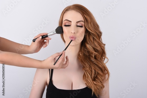 Foto Attractive, shapely model with long red hair being made-up in the studio
