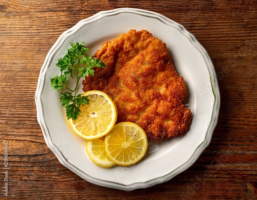 golden crispy wiener schnitzel served on a white plate with lemon wedges and parsley garnish arranged on a wooden table background