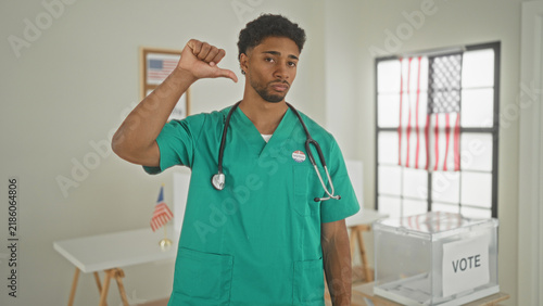 Bild auf Leinwand Man doctor in green scrubs with stethoscope showing thumbs down beside ballot box in a polling building; disapproval civic duty