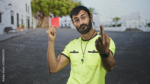 Obraz na płótnie Man referee holding red card and showing middle finger on a street with whistle and headset visible; defiance