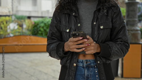 Young woman holding smartphone and texting, hands and midriff visible on an urban street; calm connection.