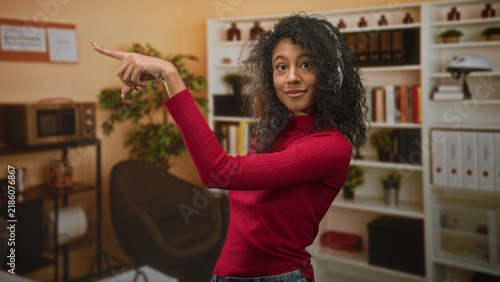 Foto Teenage woman in red sweater wearing headphones pointing finger and nodding to music in studio; playful joy