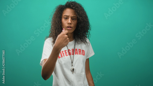Foto Woman lifeguard pointing finger with raised hand and whistle on lanyard in studio; concern vigilance