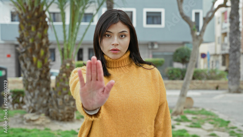 Foto Woman shows palm forward stop gesture on street wearing yellow turtleneck sweater; boundary assertiveness determination