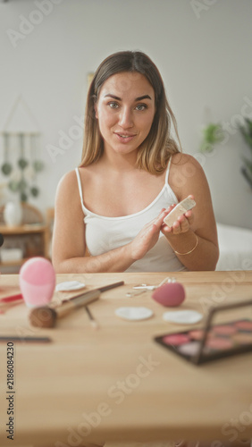Foto Young woman holds makeup brush in hand and smiles at camera at a vanity table with beauty tools in studio; confidence