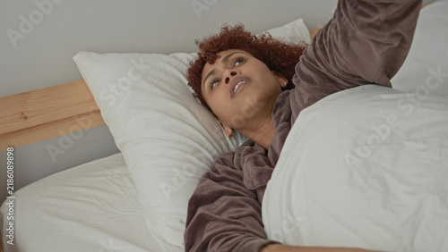 Quadro su tela Woman covering ears for earache while clutching white duvet on wooden bedframe in building; pain exhaustion