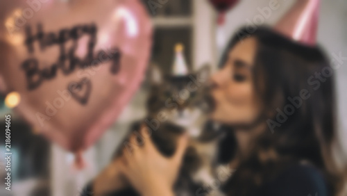 Blurred view of a woman in a party hat kissing her cat on its birthday