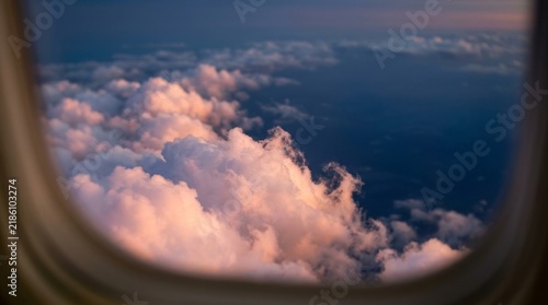 Aerial View of Fluffy White Cumulus Clouds from Airplane Window over Clear Blue Sky Background