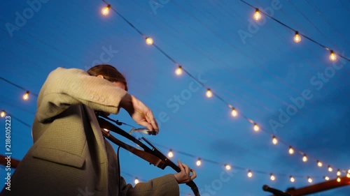 Outdoor evening string performance under festive lights with violinist and guitarist playing live music on a lakeside stage during a relaxed twilight gathering