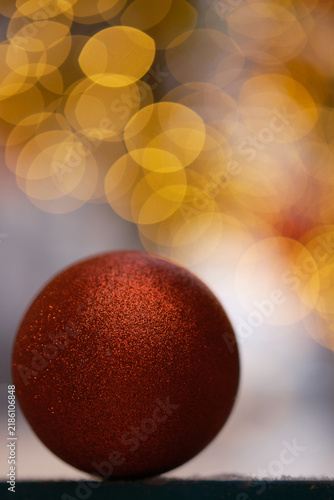  round red glitter Christmas bauble in sharp focus against a softly blurred background of warm golden bokeh lights. The ornament has a richly textured sparkling surface