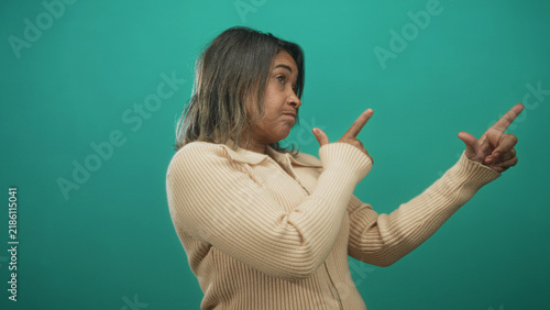 Canvastavla Hispanic middle aged woman points both index fingers in finger gun gesture in studio with teal backdrop, wearing beige sweater and shrugging expression; casual skepticism