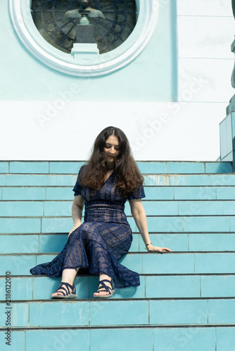Vertical full length portrait of happy woman sitting on blue stairs enjoying sunny day