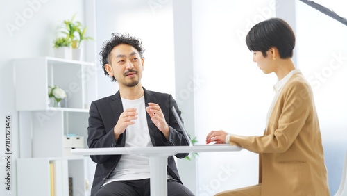 Fototapeta 明るいオフィスで手振りを交えて話す男性と記録する女性