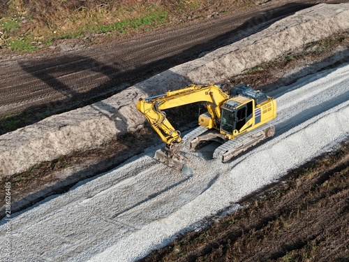 excavator spreads gravel for a new road through previously undeveloped grassland; construction site from a bird's-eye view; road construction; environment; land use; development